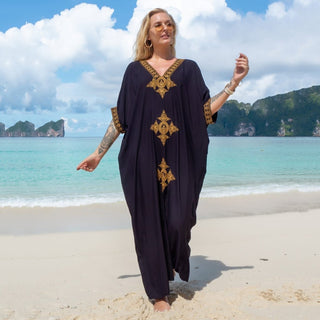 A woman wearing a black v-neck kaftan summer dress at the beach.