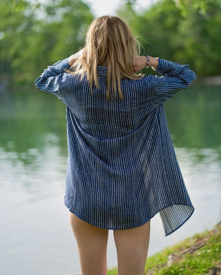 A woman wearing a blue button down  shirt cover up by the lake.