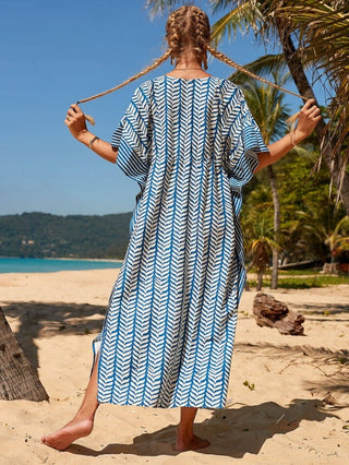 A woman wearing a blue print caftan dress with sun glasses at the beach.