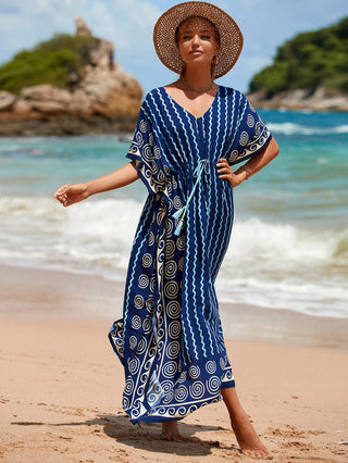 A woman wearing a dark blue stripe kaftan dress with a hat at the beach.