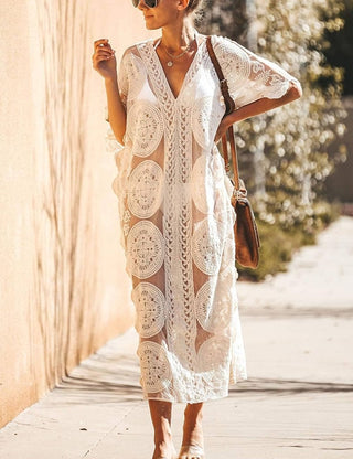 A woman wearing a short sleeve white  lace kaftan dress with a bag.