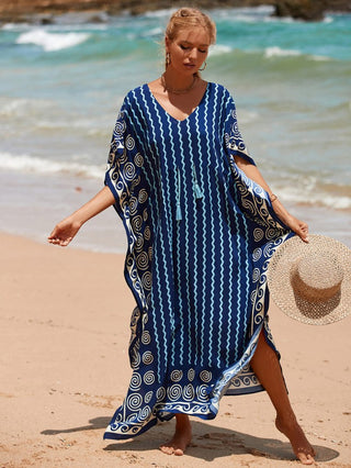 A woman wearing a stripe kaftan dress with a hat at the beach.