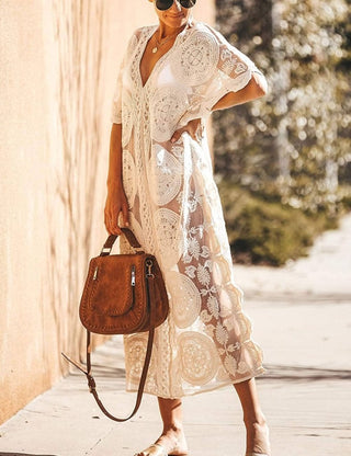 A woman wearing a white short sleeve lace kaftan dress with a bag.